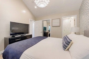 A bedroom with a bed, a television, a dresser, and a door leading to another room.