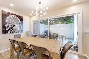A dining area with a wooden table and chairs, a large window with a view of a backyard, and a ceiling light fixture.