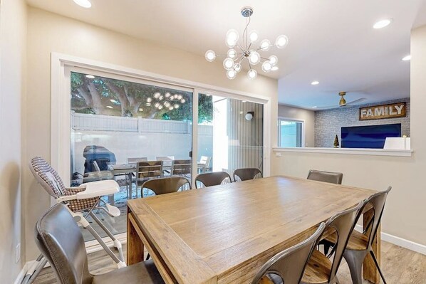 A dining area with a wooden table and chairs, a chandelier, and a 'FAMILY' sign on the wall.