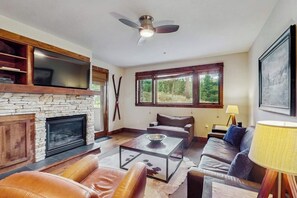 Ein Wohnzimmer mit Kamin aus Stein, Ledersofas, einem Glastisch und einem Deckenventilator.