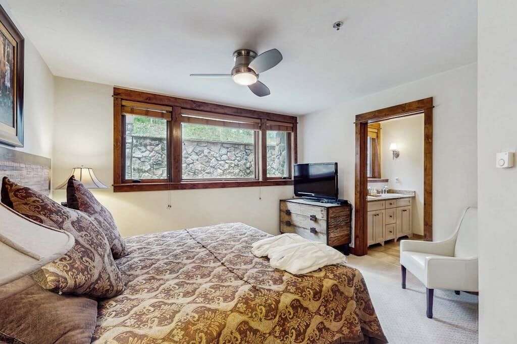 A bedroom with a bed, a television, a dresser, a chair, and a window with a view of greenery.