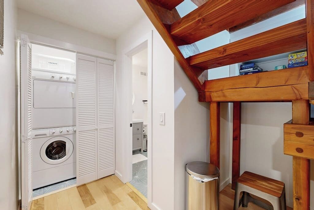 Une pièce compacte équipée d’un lave-linge et d’un sèche-linge intégrés, d’un petit tabouret et d’une poubelle.