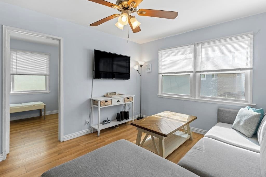 A modern living room with a ceiling fan, a flat-screen TV, a wooden coffee table, a sofa, and a bench.