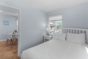 Ein Schlafzimmer mit einem Bett, einem Nachttisch, einem Fenster mit Jalousien, einem Sessel und einem Tisch mit Lampe.