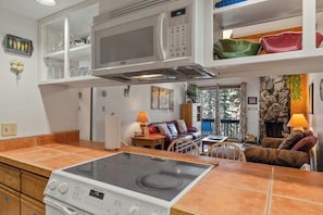 A kitchen with a stove, microwave, and cabinets, a dining area with a table and chairs, and a living room with a sofa and fireplace. - Mountain view condo in Cascade Village w/ easy access to trails (Durango)