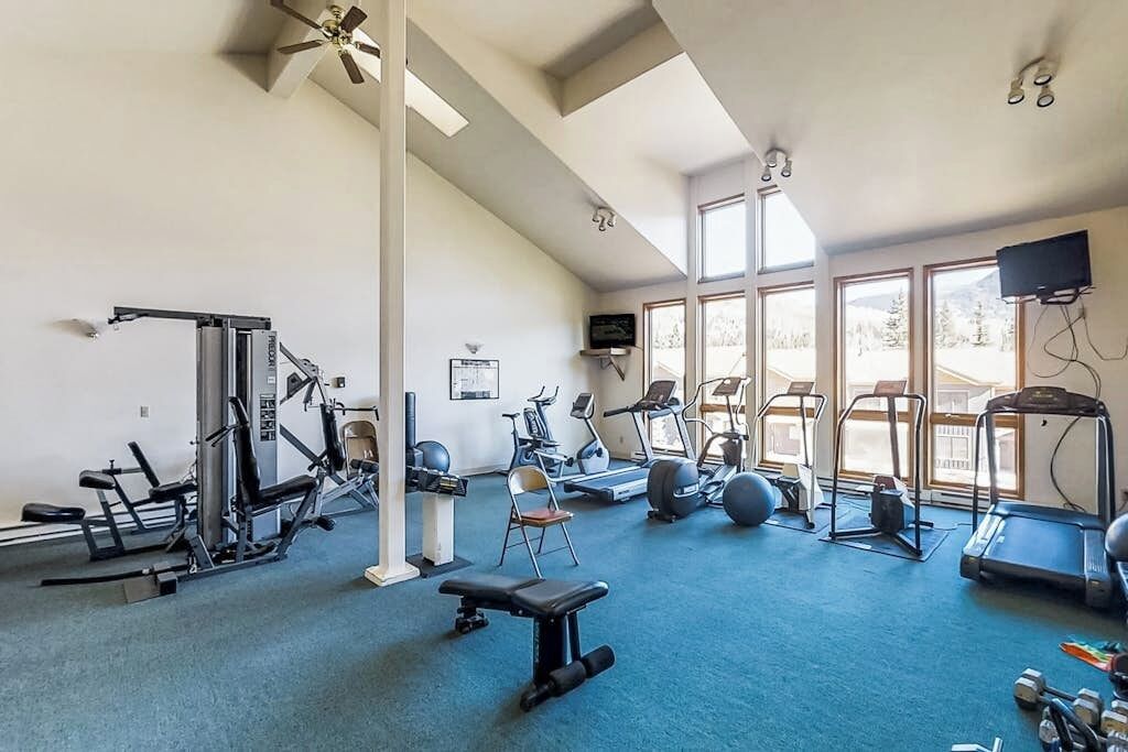 Een sportschool met trainingsapparatuur, grote ramen en een plafondventilator.