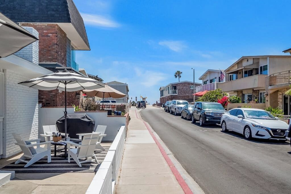 A street with parked cars, outdoor seating with umbrellas, and buildings with balconies.