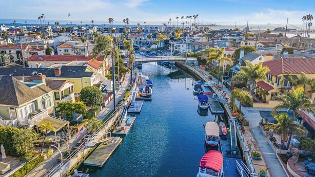 A marina with boats docked, a bridge, and residential buildings along the water. - Bright home on the channel with expansive patio & elevator (Long Beach)
