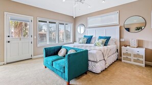 A bedroom with a bed, a blue sofa, a white bedside table, and a ceiling fan. - Bright home on the channel with expansive patio & elevator (Long Beach)