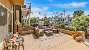 A patio with outdoor furniture, a view of a marina, and palm trees. - Bright home on the channel with expansive patio & elevator (Long Beach)