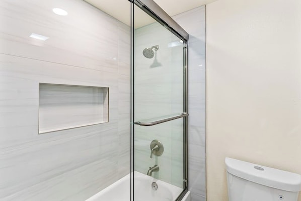 Ein modernes Badezimmer mit einer glasgeschlossenen Dusche, einer weißen Toilette und einer eingebauten Ablagefläche.
