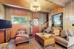 Ein gemütliches Blockhaus-Interieur mit Fernseher, zwei Sofas, einem Couchtisch und einem großen Fenster.