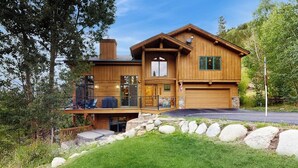 Une cabane en rondins à deux étages, dotée d’un balcon, d’un garage et d’un mur de soutènement en pierre.