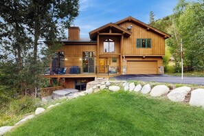 Eine zweistöckige Blockhütte mit Balkon, Garage und einer Steinmauer.