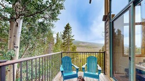 Une terrasse en bois avec deux chaises bleues, un foyer et une porte vitrée donnant sur un paysage magnifique.