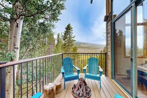 Eine Holzterrasse mit zwei blauen Stühlen, einer Feuerstelle und einer Glastür, die zu einer schönen Aussicht führt.