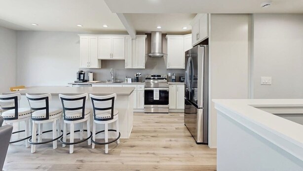 Una cocina moderna con armarios blancos, electrodomésticos de acero inoxidable y una isla central con taburetes de bar.