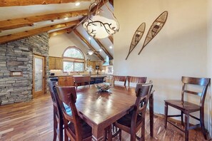 A dining area with a wooden table and chairs, a stone wall, and a kitchen in the background.