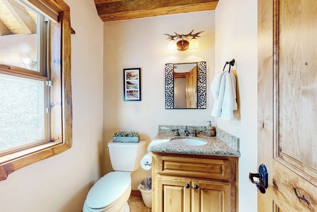 Une salle de bain comprenant des toilettes, un lavabo, des meubles en bois, un miroir et une fenêtre.