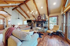 A cozy living room with a stone fireplace, wooden beams, a sofa, and a chair.