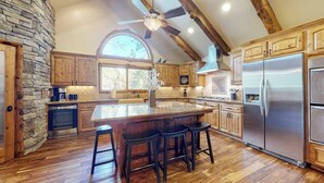 Una cocina con una isla central, armarios de madera, una pared de piedra y un ventanal grande.