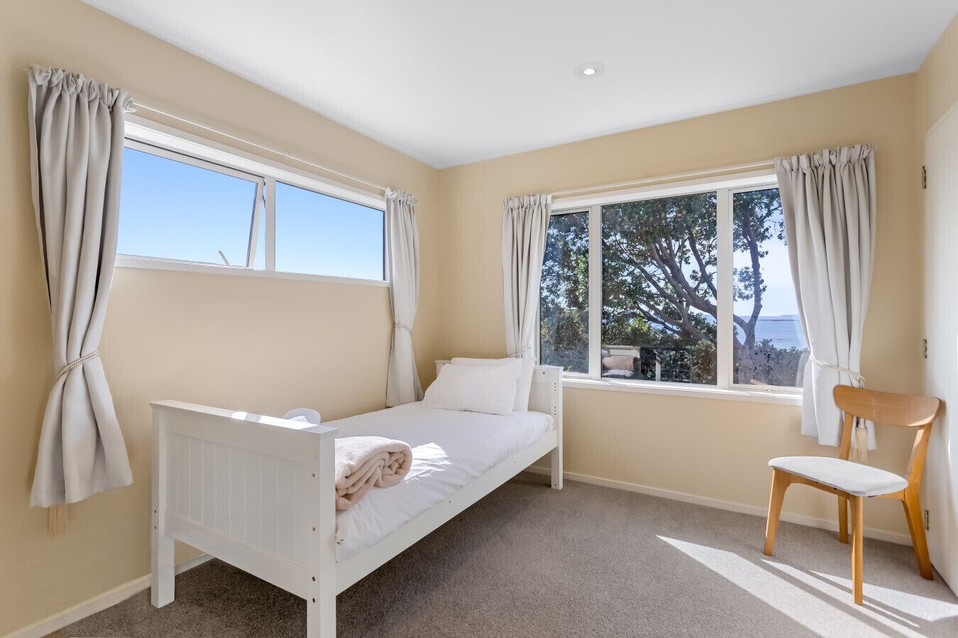 A bedroom with a single bed, a chair, and two windows with curtains.