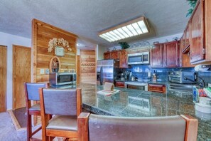 A kitchen with wooden cabinets, a refrigerator, microwave, and a glass island with chairs. - In-town condo with ideal walk-to-lifts location, pool, hot tubs & sauna (Breckenridge)