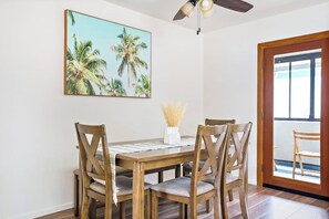 A dining area with a wooden table and chairs, a ceiling fan, and a large tropical-themed painting on the wall.