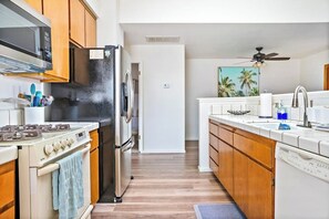 A kitchen with wooden cabinets, a stainless steel refrigerator, a stove, and a ceiling fan.