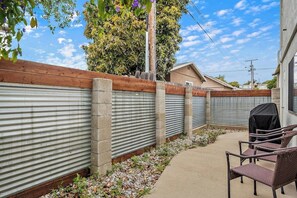 A backyard with a wooden fence, a metal gate, a barbecue grill, and outdoor furniture. - 2-story centrally located home with grill, patio, fireplace, streaming, & W/D (Grover Beach)