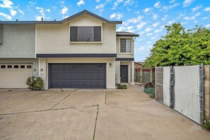 A two-story house with a garage, a fenced yard, and a tree.