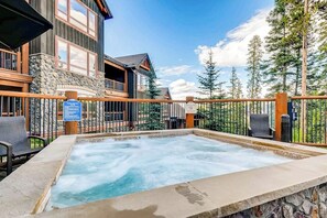 Ein Whirlpool mit Steinrand, einer Holzterrasse und Blick auf eine Lodge mit Steinwänden und großen Fenstern.