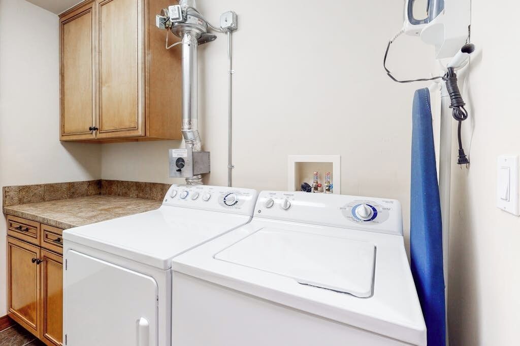 A laundry area with a front-loading washer and dryer, wooden cabinets, and a countertop.