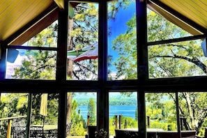 Ein Zimmer mit großen Fenstern, Blick auf Bäume und einen See, und eine Flagge mit der Aufschrift 'California' und 'Germany'.
