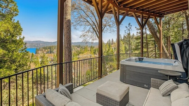 A covered outdoor seating area with a hot tub, overlooking a forested landscape and a body of water. - Incredible Lake View, Private Hot Tub, Huge Game Room, A/C,-Short Walk to Lake (Lake Arrowhead)