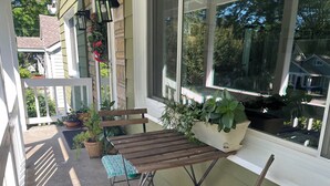 Un porche cubierto con una mesa de madera y dos sillas, plantas en macetas y vistas del barrio.
