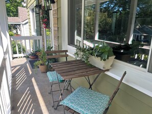 Eine überdachte Veranda mit Holztisch und zwei Stühlen, Blumentöpfen und Blick auf die Nachbarschaft.