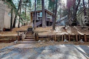 Eine Holzhütte mit einer Holztreppe, die zu einer Terrasse führt, umgeben von Bäumen.