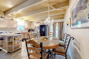 A spacious kitchen with wooden cabinets, a dining table with chairs, a chandelier, and a large window. - Dog-friendly rural home with deck, wood fireplace, fast WiFi, patio & gas grill (Crestline)