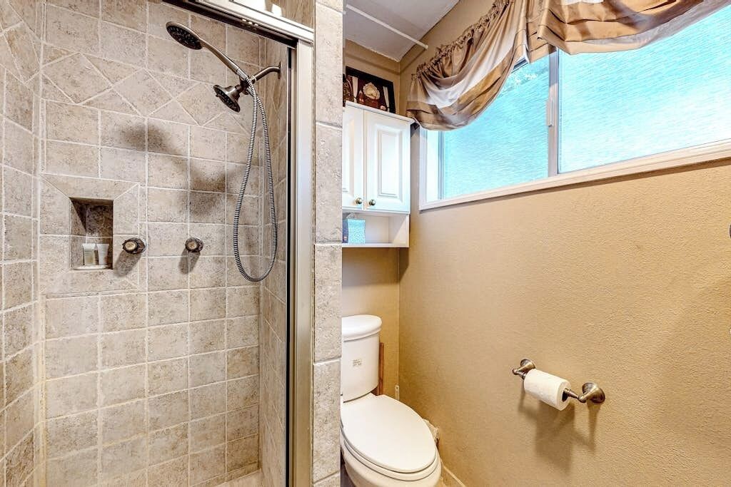 Un baño con ducha, inodoro y ventana con cortinas.