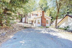 A two-story house with a brick chimney, a fenced driveway, and a surrounding wooded area. - Dog-friendly rural home with deck, wood fireplace, fast WiFi, patio & gas grill (Crestline)