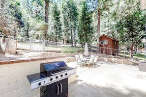An outdoor patio with a grill, chairs, and a small wooden structure. - Dog-friendly rural home with deck, wood fireplace, fast WiFi, patio & gas grill (Crestline)