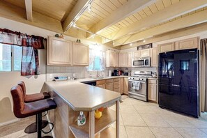 Una cocina con armarios de madera, un refrigerador negro, un microondas, una estufa y una barra con taburetes.
