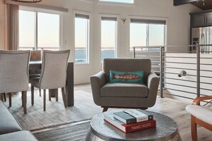 Ein modernes Wohnzimmer mit Sofa, Sessel, Esstisch und Büchern auf einem Couchtisch.