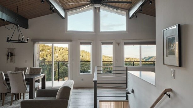 Une pièce spacieuse avec un plafond haut, de grandes fenêtres, un escalier et un coin repas.
