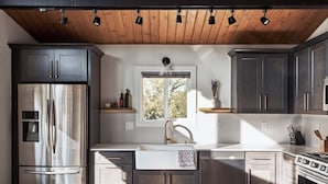 Une cuisine moderne avec des meubles de couleur sombre, des appareils électroménagers en acier inoxydable et un plafond en bois.