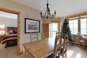 A dining area with a wooden table and chairs, a chandelier, a framed picture on the wall, and a Christmas tree. - Cozy Mountain Condo with Pool & Hot Tub - Close to the Slopes (Keystone)