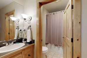 A bathroom with a wooden vanity, a large mirror, two wall-mounted hair dryers, and a striped shower curtain. - Cozy Mountain Condo with Pool & Hot Tub - Close to the Slopes (Keystone)