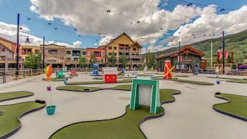 A resort area with a central building, a pool with a green deck, and surrounding buildings.
