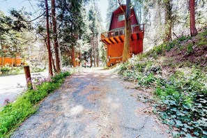 A rustic cabin with a balcony, surrounded by dense forest and a gravel path. - Dog-friendly 2-story home with large deck, tree views, fireplace, & W/D (Crestline)